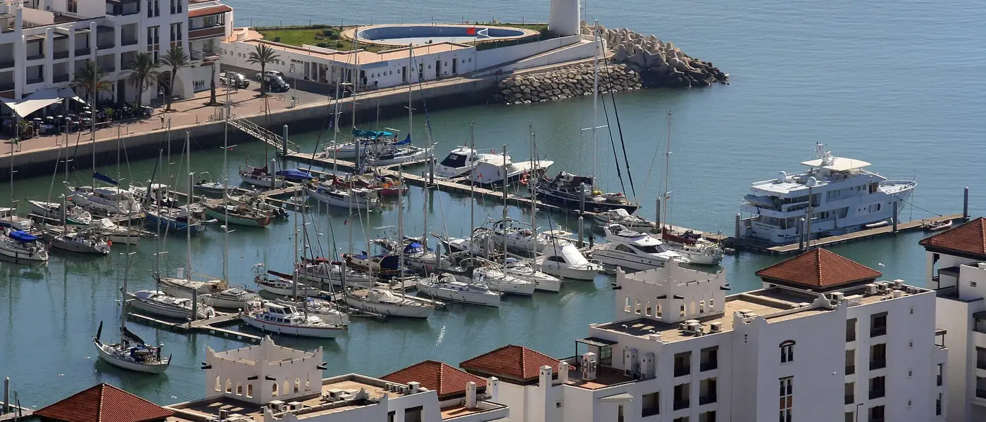 Yachts moored in Agadir Marina beside white buildings and the harbour wall