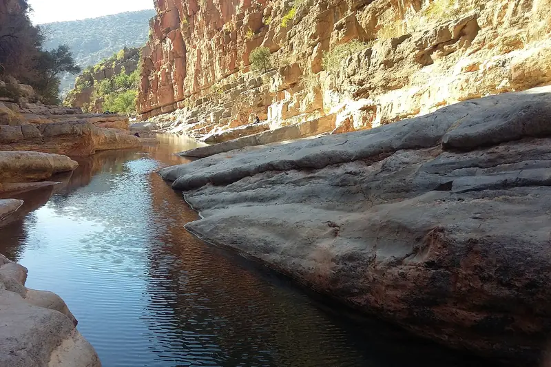 Clear water pool between smooth rocks and red cliffs in Paradise Valley