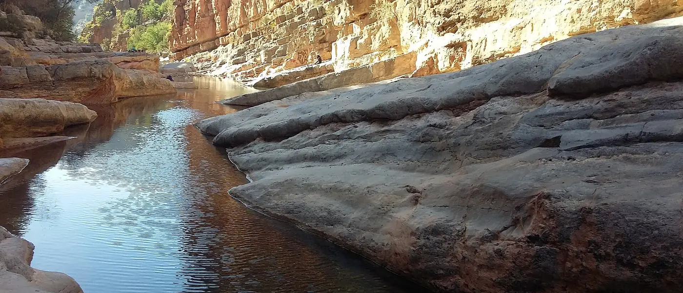 Clear water pool between smooth rocks and red cliffs in Paradise Valley